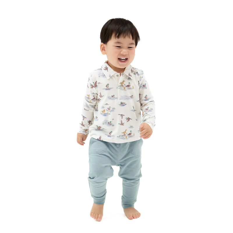 Child wearing a patterned shirt and light blue pants on a white background