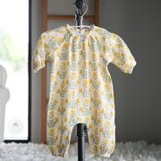 Baby onesie with yellow floral pattern hanging on a hook against a neutral background