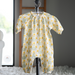 Baby onesie with yellow floral pattern hanging on a hook against a neutral background