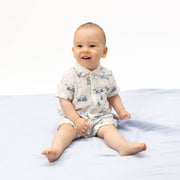 Baby sitting on a white blanket wearing a patterned outfit.