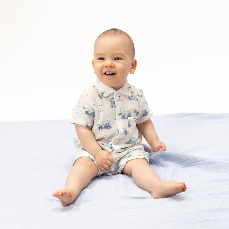 Baby sitting on a white blanket wearing a patterned outfit.