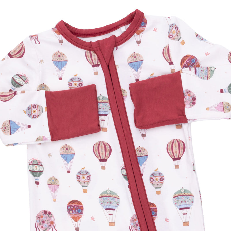 A baby long-sleeve sleep sack with a white background printed with colorful hot air balloon motifs, featuring solid red trim, a red front zipper, and two red patch pockets on the sleeves.
