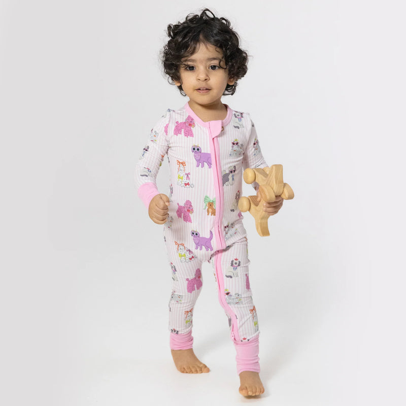 Child wearing a patterned onesie holding a wooden toy on a white background