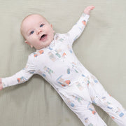 Baby wearing a white onesie with colorful patterns on a beige blanket