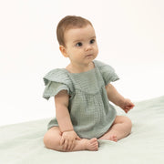 Baby wearing a light green dress sitting on a white surface