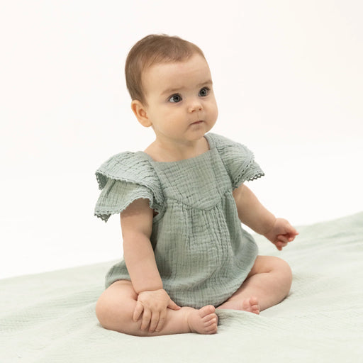 Baby wearing a light green dress sitting on a white surface