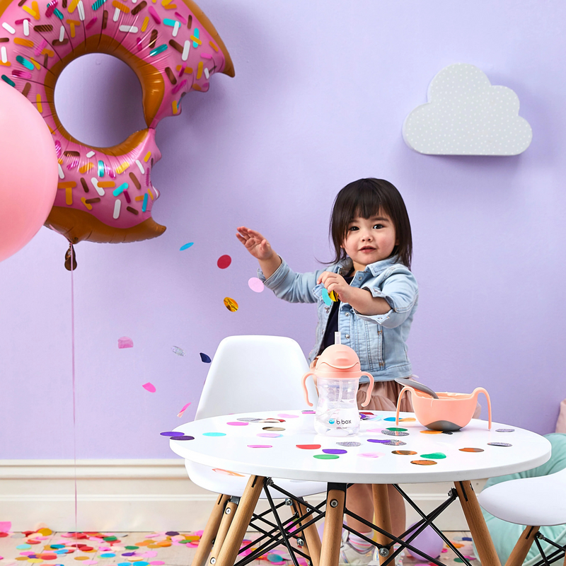 Child playing with toys at a table in a room with colorful balloons and a purple wall.