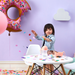 Child playing with toys at a table in a room with colorful balloons and a purple wall.