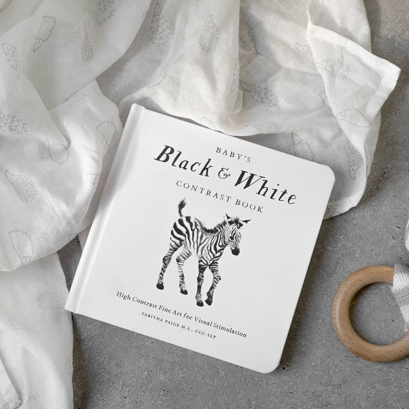 Baby book titled 'Black & White Contrast Book' with a zebra illustration, placed on a soft fabric background.
