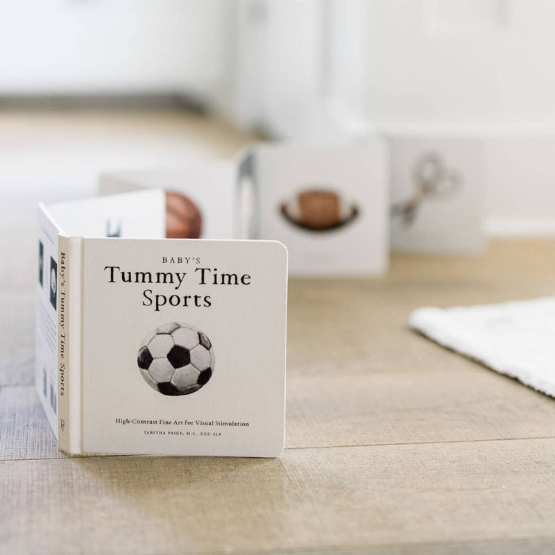 Children's book titled 'Tummy Time Sports' on a wooden surface with a blurred background
