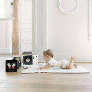 Baby lying on a white rug in a minimalistic room with white walls and wooden floor.
