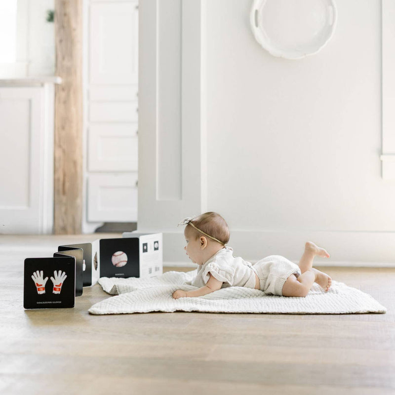 Baby lying on a white rug in a minimalistic room with white walls and wooden floor.