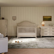 Nursery room with wooden crib, dresser, and lamp against striped wall.