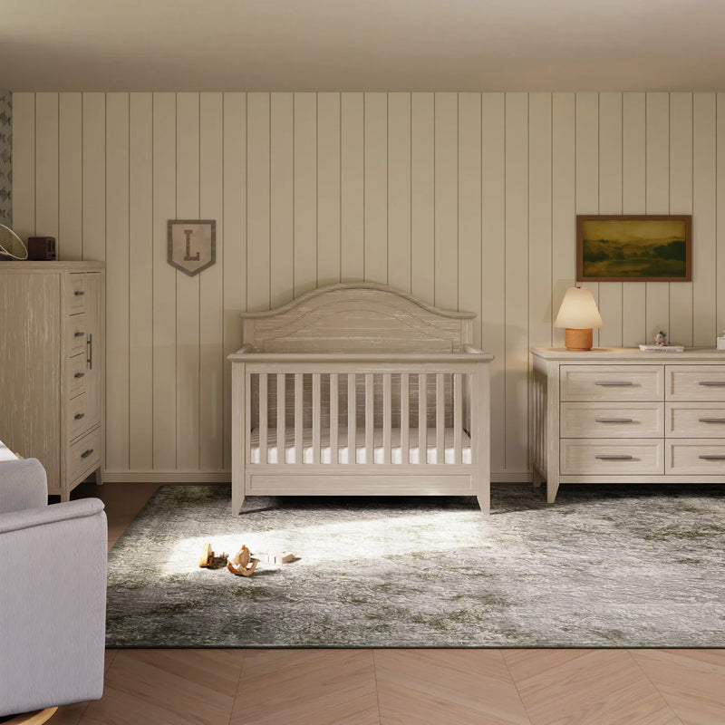 Nursery room with wooden crib, dresser, and lamp against striped wall.