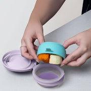 Hands opening a colorful food container with compartments on a light surface