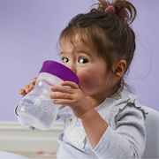 Child drinking from a purple sippy cup against a light purple background