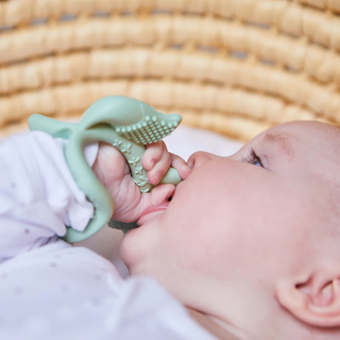 Baby holding a green teething ring against a woven background