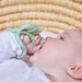 Baby holding a green teething ring against a woven background