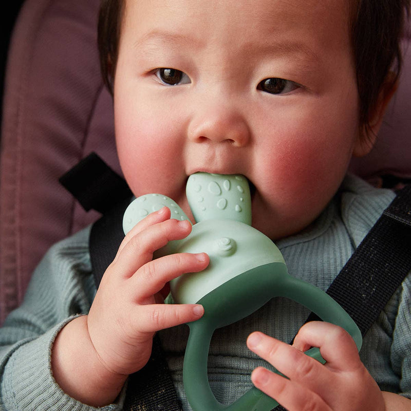 Baby holding a green teething toy with a blurred background