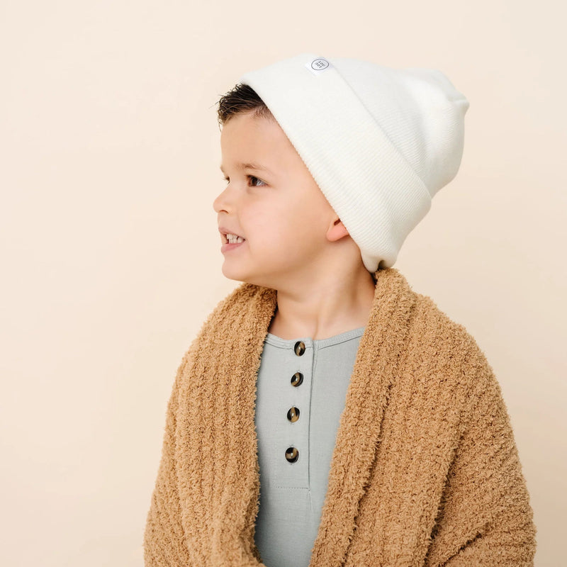Child wearing as ivory beanie and beige cardigan on a beige background