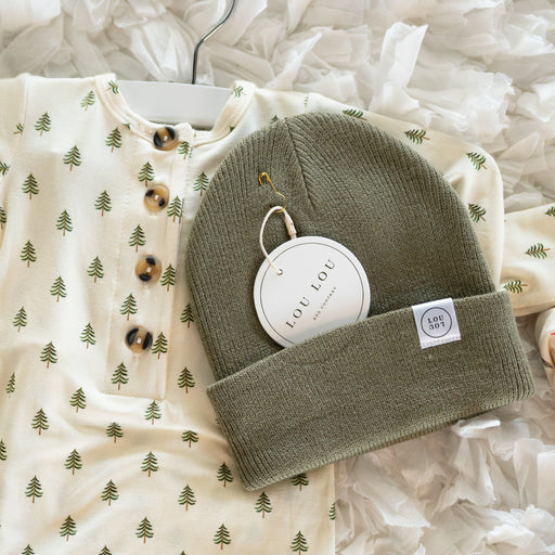Baby outfit with long-sleeve shirt and green beanie on a textured white surface