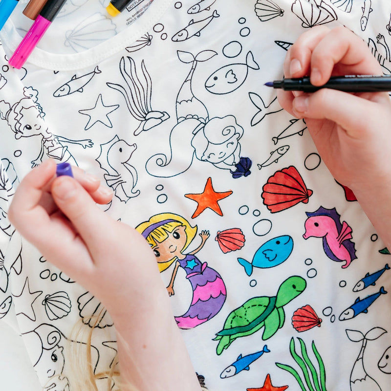Close-up of hands coloring mermaid and ocean illustrations on colorable pajama fabric