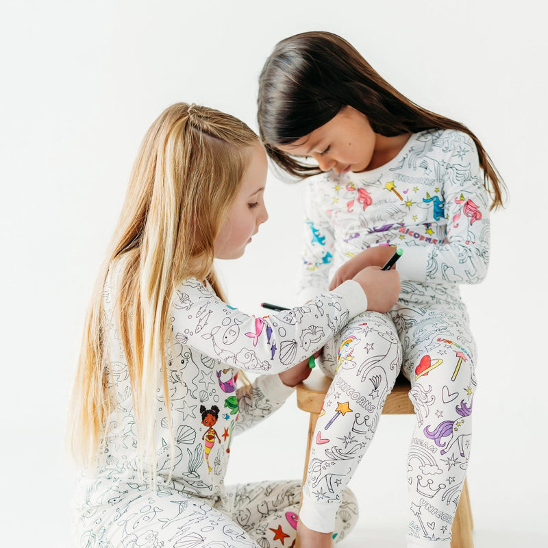 Two children sitting together coloring their Bee Colorful Co mermaid colorable pajamas