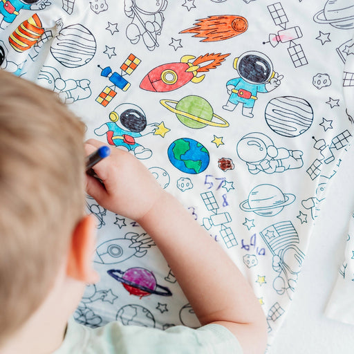 Overhead view of child coloring the space-themed pajama fabric with bright marker designs