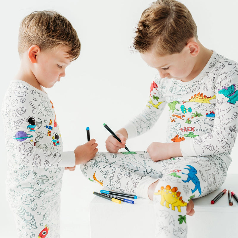 Two children coloring Bee Colorful Co space pajamas together at a table