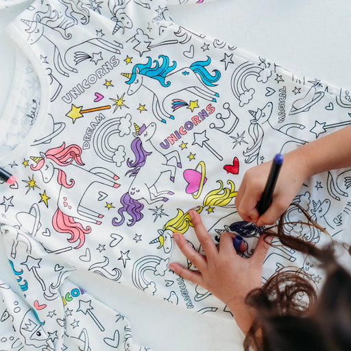Child coloring unicorn and rainbow designs on pajama top with fabric markers