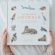 Person holding a book titled 'Our Big Book of Animals' with illustrations of various animals on the cover.