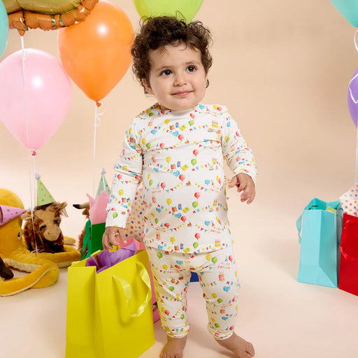 Toddler wearing Birthday Babe magnetic pajamas standing with balloons and gifts