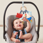 Baby seated in a car seat reaching for the Bitzy Busy Ring activity toy