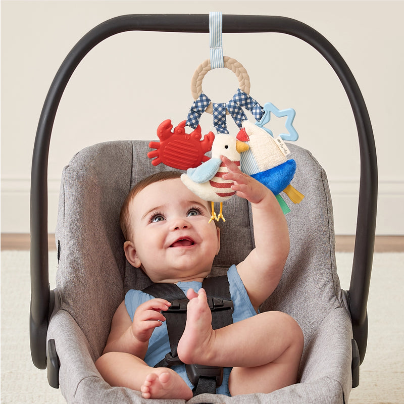 Baby seated in a car seat reaching for the Bitzy Busy Ring activity toy
