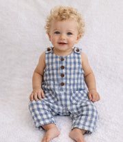 Baby wearing a blue checkered romper sitting on a white textured surface