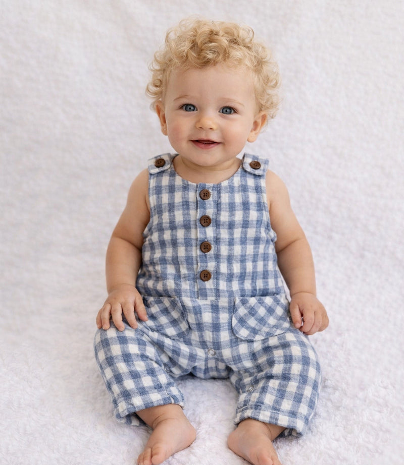 Baby wearing a blue checkered romper sitting on a white textured surface