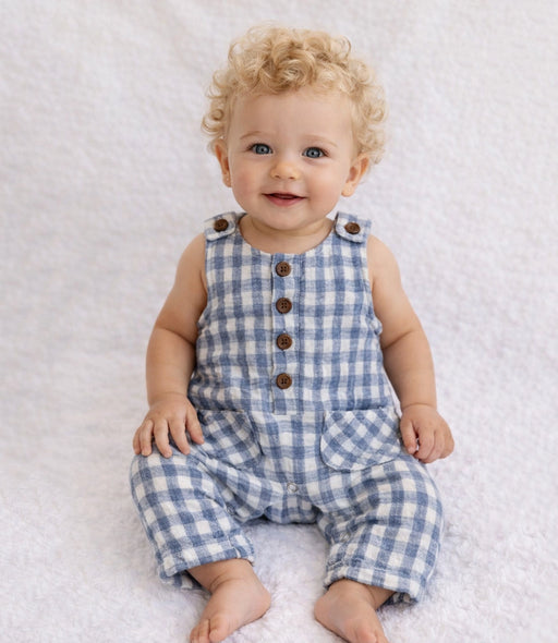 Baby wearing a blue checkered romper sitting on a white textured surface