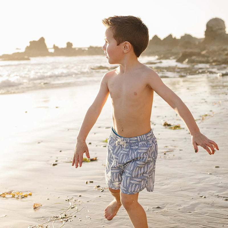 Young boy walking on a sandy beach with a cityscape in the background