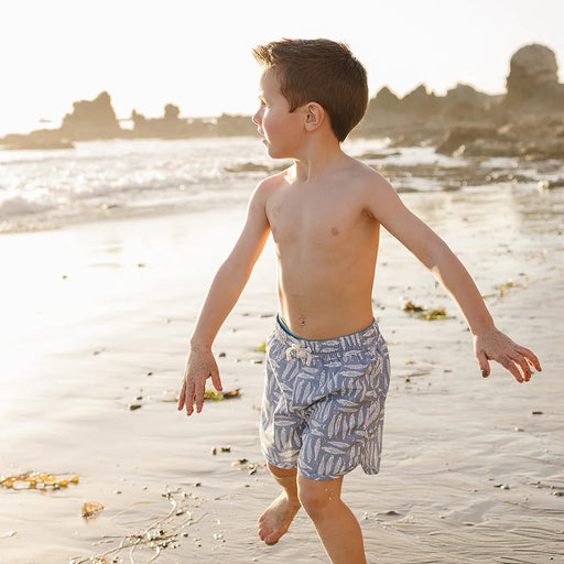 Young boy walking on a sandy beach with a cityscape in the background
