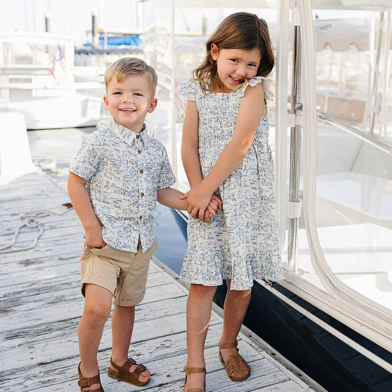 Two children holding hands on a dock with boats in the background