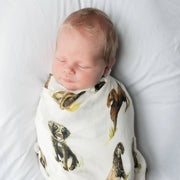 Newborn wrapped in Saltwater Swaddles Boykin Spaniel swaddle with watercolor Boykin dogs printed across soft white fabric