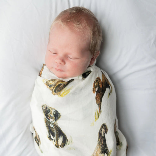 Newborn wrapped in Saltwater Swaddles Boykin Spaniel swaddle with watercolor Boykin dogs printed across soft white fabric