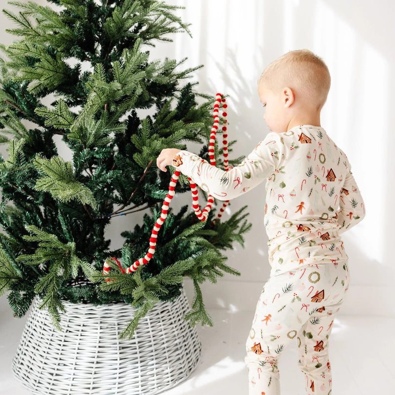 Child in pajamas decorating a Christmas tree with red and gold ornaments on a white background