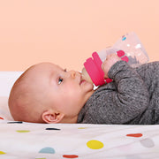 Baby lying on a colorful polka dot blanket, holding a pink sippy cup.