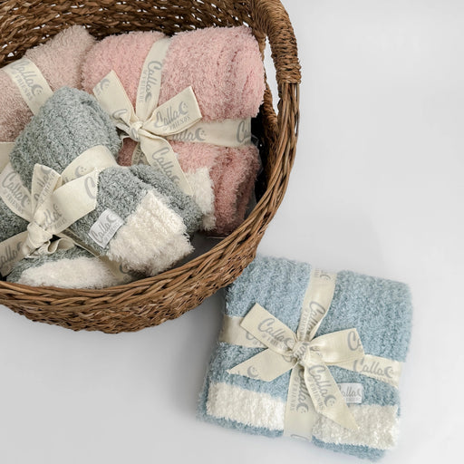 Basket filled with sage, petal pink, and powder blue Alani blankets tied with cream ribbons