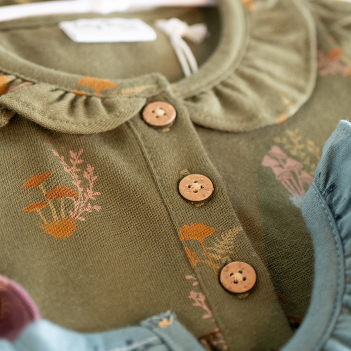 Close-up of a green children's outfit with floral patterns and buttons.