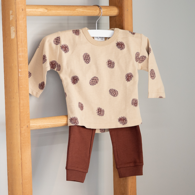 Children's beige shirt with pine cone pattern and brown pants hanging on a wooden rack.