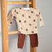 Children's beige shirt with pine cone pattern and brown pants hanging on a wooden rack.