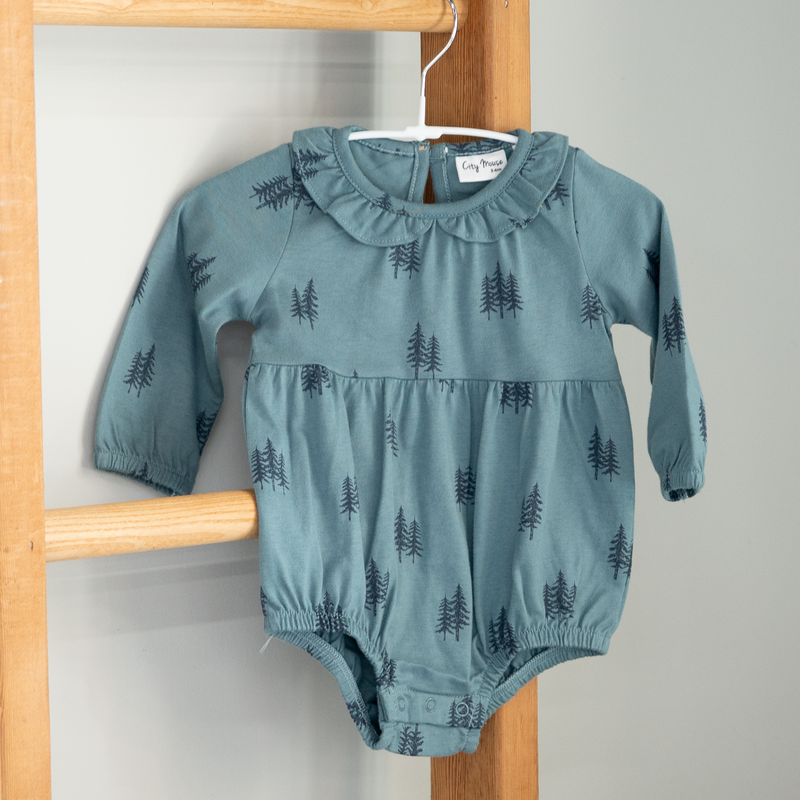 Blue baby romper with tree pattern hanging on a wooden rack.