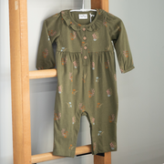 Green baby romper with floral patterns on a wooden hanger against a gray wall.